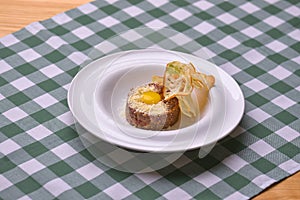 Close up of beef tartar with capers and small toasts. Served on a white plate over green plaid tablecloth background.