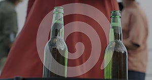 Close-up of beer bottles at outdoor party and female hand taking and drinking having fun with friends