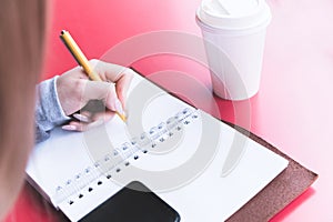 Close-up from behind the back of a young woman in a winter polto is holding a ballpoint pen and is going to write