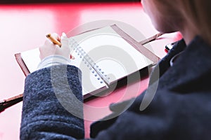 Close-up from behind the back of a young woman in a winter polto is holding a ballpoint pen and is going to write