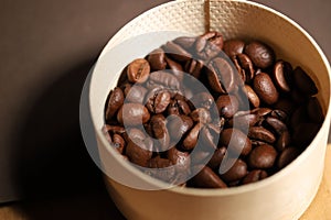 Close up of a beige wicker container filled with coffee beans on a wooden table