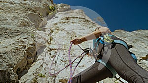 CLOSE UP: Belayer creates slack in rope attached to climber scaling a cliff.