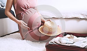 Close-up belly of pregnant woman with travel bag of clothes and necessities. Mother during pregnancy preparing and packing photo