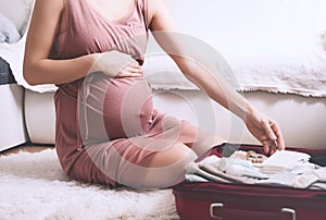 Close-up belly of pregnant woman with travel bag of clothes and necessities. Mother during pregnancy preparing and packing photo