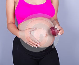 close-up belly of pregnant woman with red apple on gray background