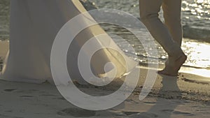 Close up below of the body, Bride and Groom are holding and walking on the beach beside the sea and wave in the Twilight time