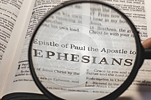 closeup of the epistle of Paul to the Ephesians from Bible using a magnifying glass to enlarge print. photo