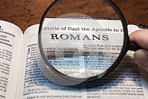 closeup of the epistle of Paul to the Romans from Bible using a magnifying glass to enlarge print. photo