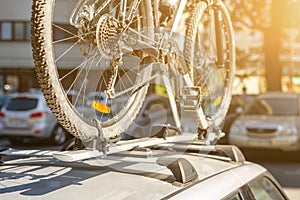 Close-up bicycle on car roof rack railing at outdoor parking. Vehicle with mounted bike on rooftop. Active sport touristic trip co