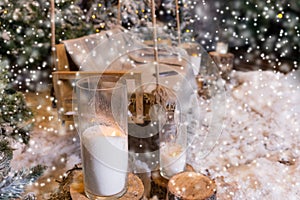 Close up of big candles in glass vases near fir-tree while snowing