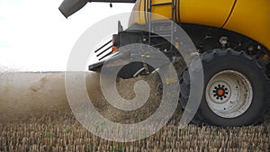 Close up of big combine wheel slowly spinning and riding at field. Harvester working in countryside, gathering crop of