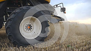 Close up of big combine wheel slowly spinning and riding at field. Harvester working in countryside, gathering crop of