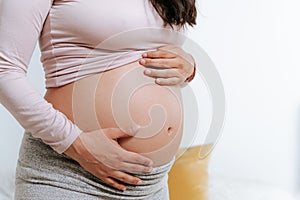 Close up of big expecting belly of pregnant woman in bed with hands touching. pregnancy, motherhood and expectation concept