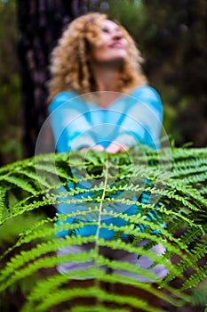 Close up of big green natural beautiful leaf holded from a cheerful and happy people caucasian woman in background - concept of