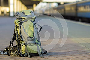 Close-up of big green tourist backpack on railway station platform on blurred background. Traveling, adventure and recreation