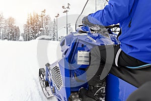 Close-up big modern snow mobile scooter atv vehicle forest road against sunrise sunny sky on cold snowy winter day