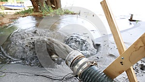 Close-up big pipe of power pump machine pouring mud sludge waste water with sand and silt on ground. Sand-wash and coast