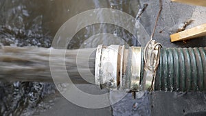 Close-up big pipe of power pump machine pouring mud sludge waste water with sand and silt on ground. Sand-wash and coast