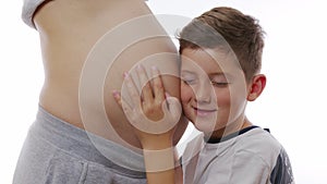 Close up of the big pregnant belly and small boy touching it. White wall background.