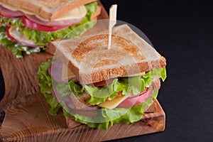 Close-up big sandwich with ham, cheese, tomatoes and salad on toasted bread on a dark background