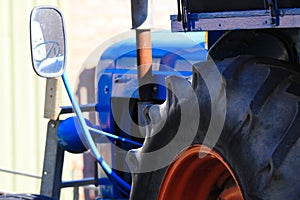 Close up of big tire of blue old ancient  antique tractor with rear view mirror and engine on a farm in Netherlands