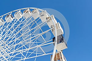 Close-up big white modern ferris wheel against clear blue sky on background in Kiev city center. One black gondola among other.