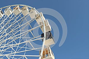 Close-up big white modern ferris wheel against clear blue sky on background in Kiev city center. One black gondola among other.