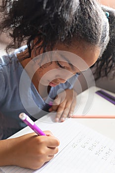 Close-up of biracial elementary schoolgirl solving mathematics sums on book at desk in classroom