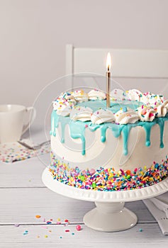 Close up of Birthday cake with vanilla icing, birthday candle and colorful sprinkles on grey white background