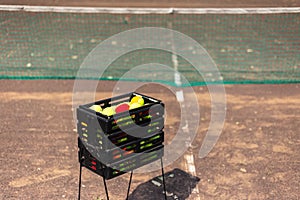 Close-up of black basket with tennis balls on court.