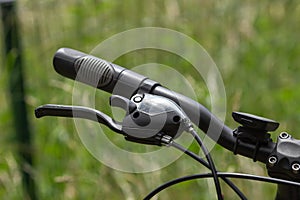 Close-up of black bicycle handlebar with brakes. Mountain sport bicycle on the green nature background. Tourism concept.