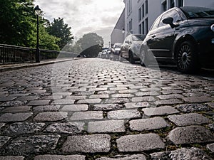 Close-up black cabbled stone road with reflection of light. Dark gray stone texture. Perspective of a road with parked