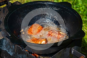 Close-up in a black cast-iron cauldron on the fire boils vegetable oil and tasty pieces of pork ribs are fried. Food in nature.