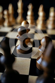 Close up of black chess pieces on board. Two rows of wooden figures on chessboard on black background. Concept of