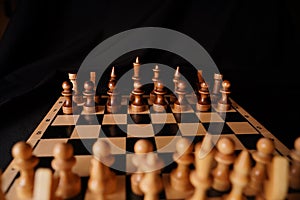 Close up of black chess pieces on board. Two rows of wooden figures on chessboard on black background. Concept of