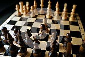 Close up of black chess pieces on board. Two rows of wooden figures on chessboard on black background. Concept of