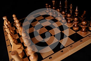 Close up of black chess pieces on board. Two rows of wooden figures on chessboard on black background. Concept of