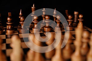Close up of black chess pieces on board. Two rows of wooden figures on chessboard on black background. Concept of