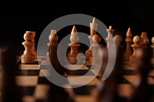 Close up of black chess pieces on board. Two rows of wooden figures on chessboard on black background. Concept of