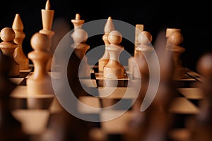 Close up of black chess pieces on board. Two rows of wooden figures on chessboard on black background. Concept of