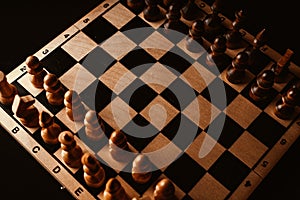 Close up of black chess pieces on board. Two rows of wooden figures on chessboard on black background. Concept of