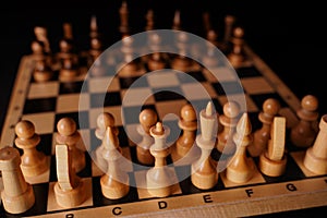 Close up of black chess pieces on board. Two rows of wooden figures on chessboard on black background. Concept of