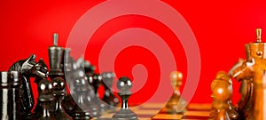 Close up of black chess pieces on board. Two rows of wooden figures on chessboard on red background. Concept of