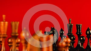 Close up of black chess pieces on board. Two rows of wooden figures on chessboard on red background. Concept of