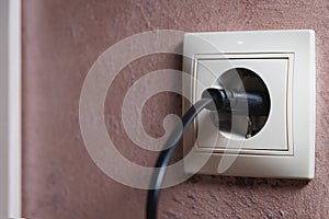 Close-up of a black electric plug in a 220 socket in the wall. Power on concept