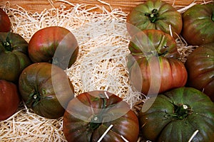 Close up of black and green ripe fresh tomatoes in wood fruit box on paper shreds cushion on French market - Provence, France