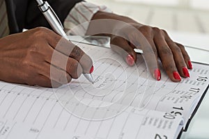 Close-up Of black hands Writing Schedule In Calendar Diary