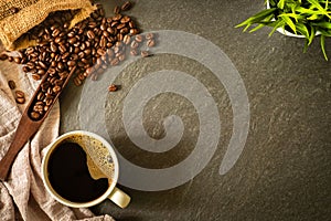 Close-up of Black hot coffee for morning with milk foam in white ceramic cup and napkin with coffee beans roasted in sack on dark