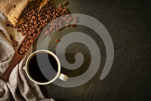 Close-up of Black hot coffee for morning with milk foam in white ceramic cup and napkin with coffee beans roasted in sack on dark