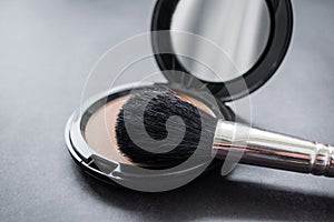 Close-up of a black makeup brush. On the background of an open box with pink powder. Dark, almost black background. Copy space